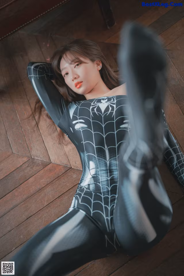 A woman in a black and white spider suit laying on the floor.