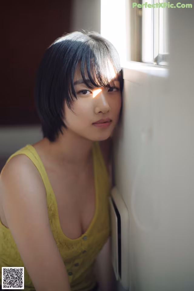 A woman leaning against a wall next to a window.