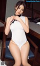 A woman in a white bodysuit sitting on a chair.