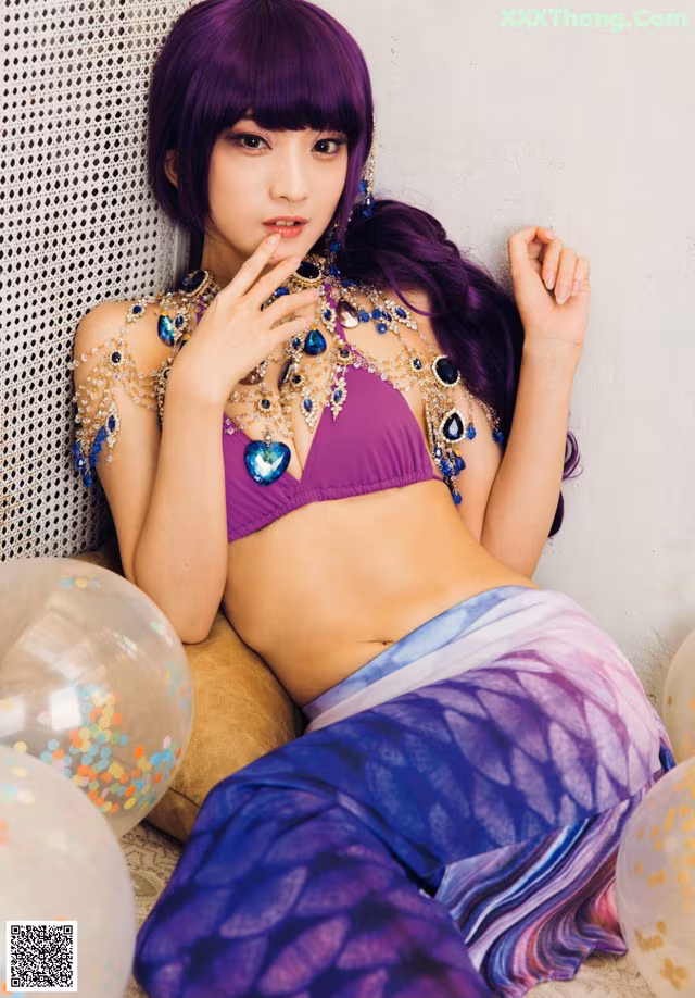 A woman in a purple bikini sitting on a couch with balloons.