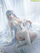 A woman in a white corset and stockings sitting on a bed.
