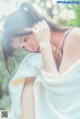 A woman wrapped in a white towel sitting on a rock.