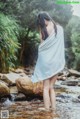 A woman standing in a stream wrapped in a towel.