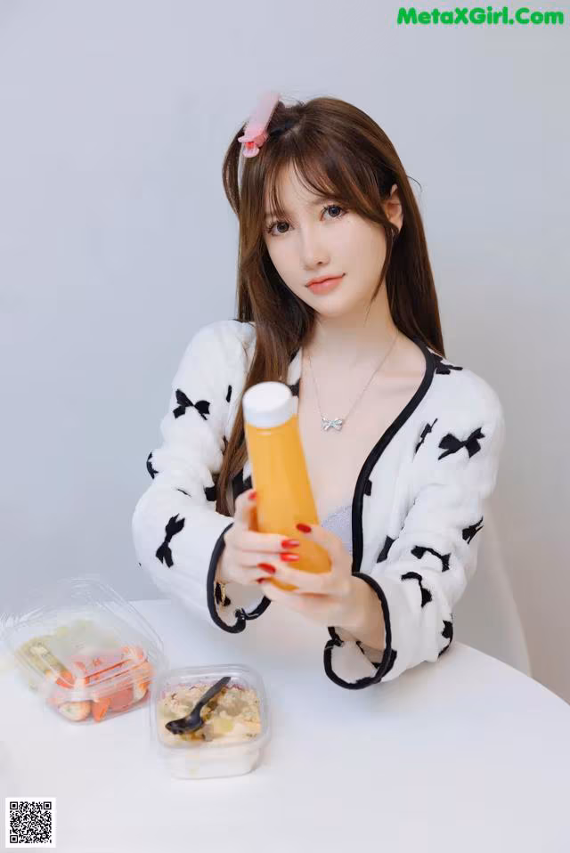 A woman sitting at a table holding a bottle of orange juice.