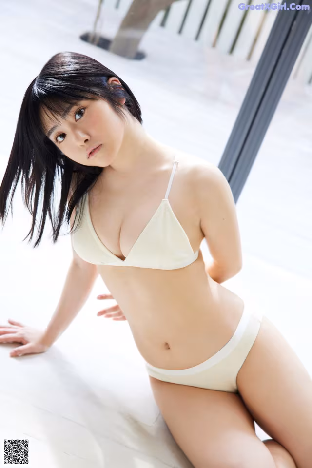 A woman in a white bikini sitting on the floor.
