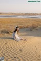 A woman sitting on top of a sand dune in the desert.