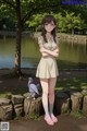 A girl standing next to a pond with a bird on her shoulder.