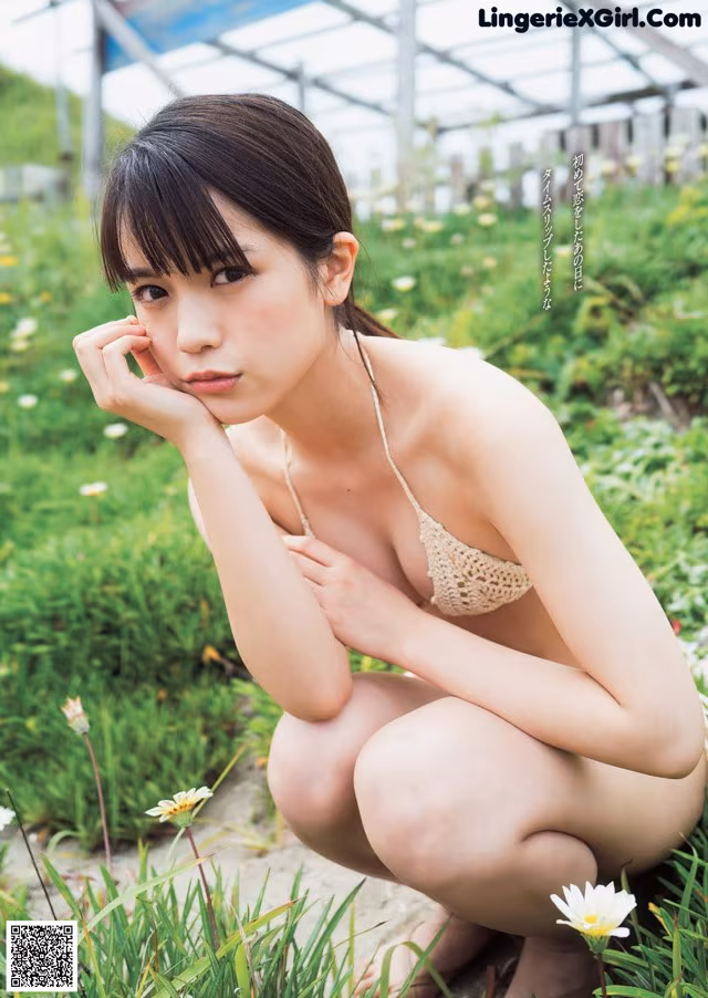A woman in a bikini sitting in a field of flowers.