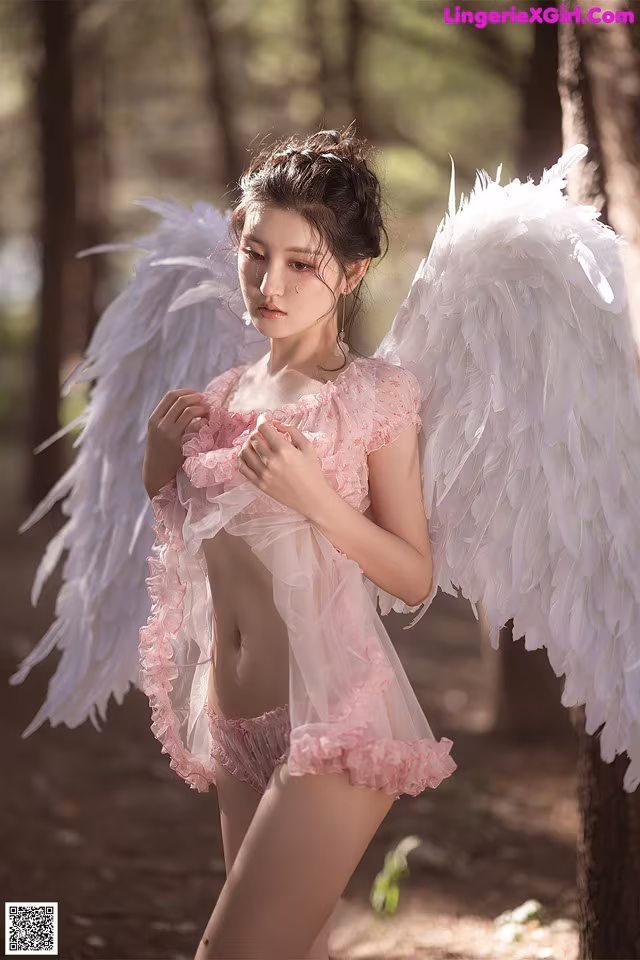 A woman in a pink dress with white wings in the woods.