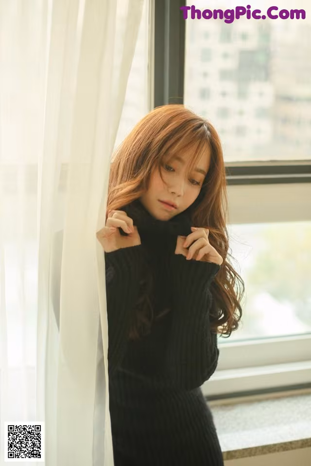 A woman in a black sweater leaning against a window.