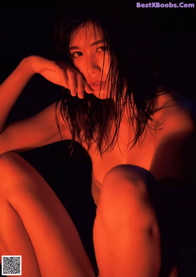 A naked woman sitting on the ground in the dark.