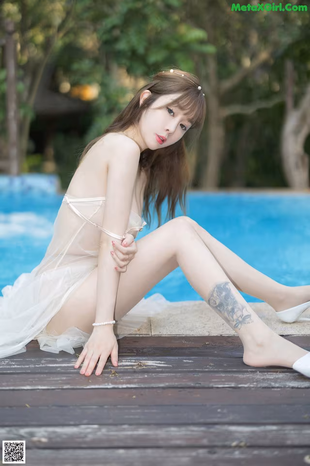 A woman in a white dress sitting by a pool.