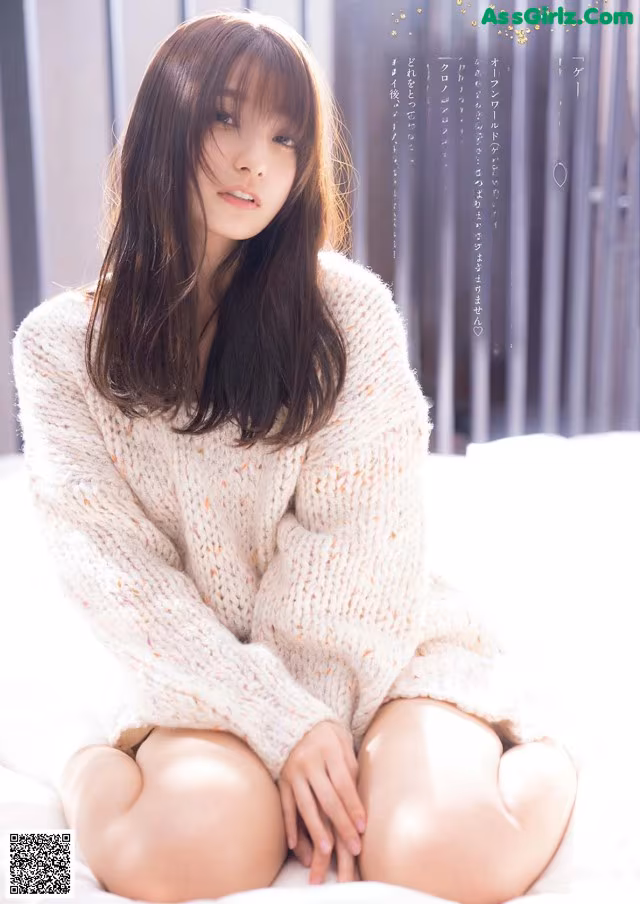 A woman sitting on top of a bed in a white sweater.