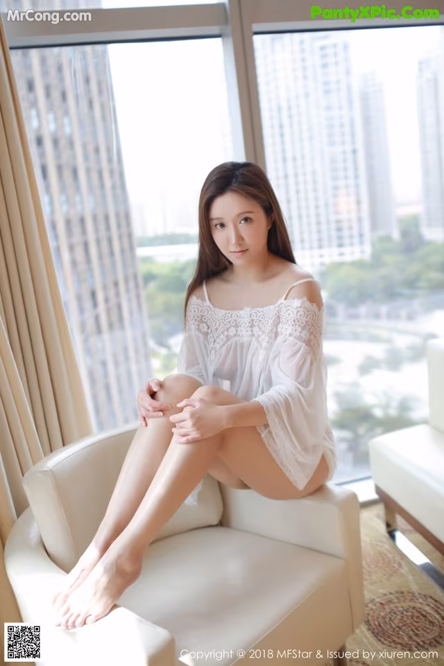 A woman sitting on a white chair in front of a window.