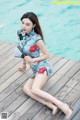 A woman sitting on a wooden dock holding a fan.