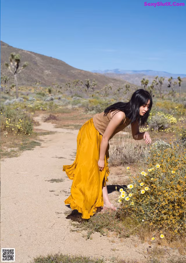 A woman in a yellow dress standing in a field of flowers.